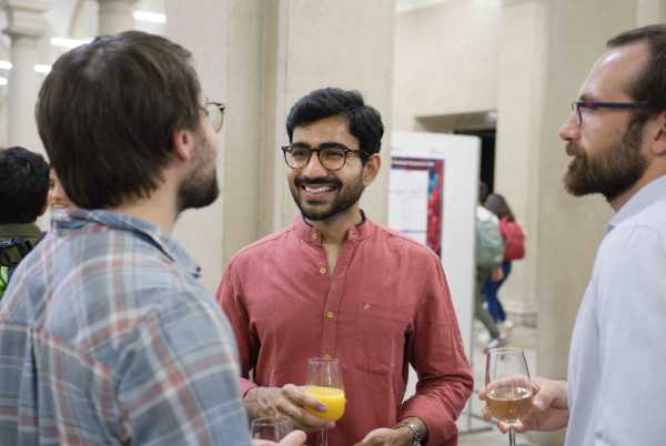 Three men seen from the chest up talking to each other. One is holding a glass of orange juice.