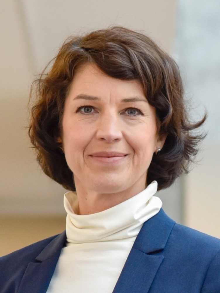 Portrait of a woman in a blue blazer and a white turtleneck. Her brown hair is chin-length.