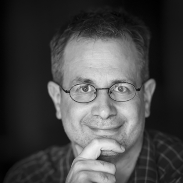 Black-and-white headshot of a caucasion man with glasses, a finger resting on his chin