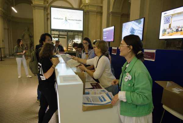 The registration desk seenfrom the side. About 5 people standing behind i, two seen checking in