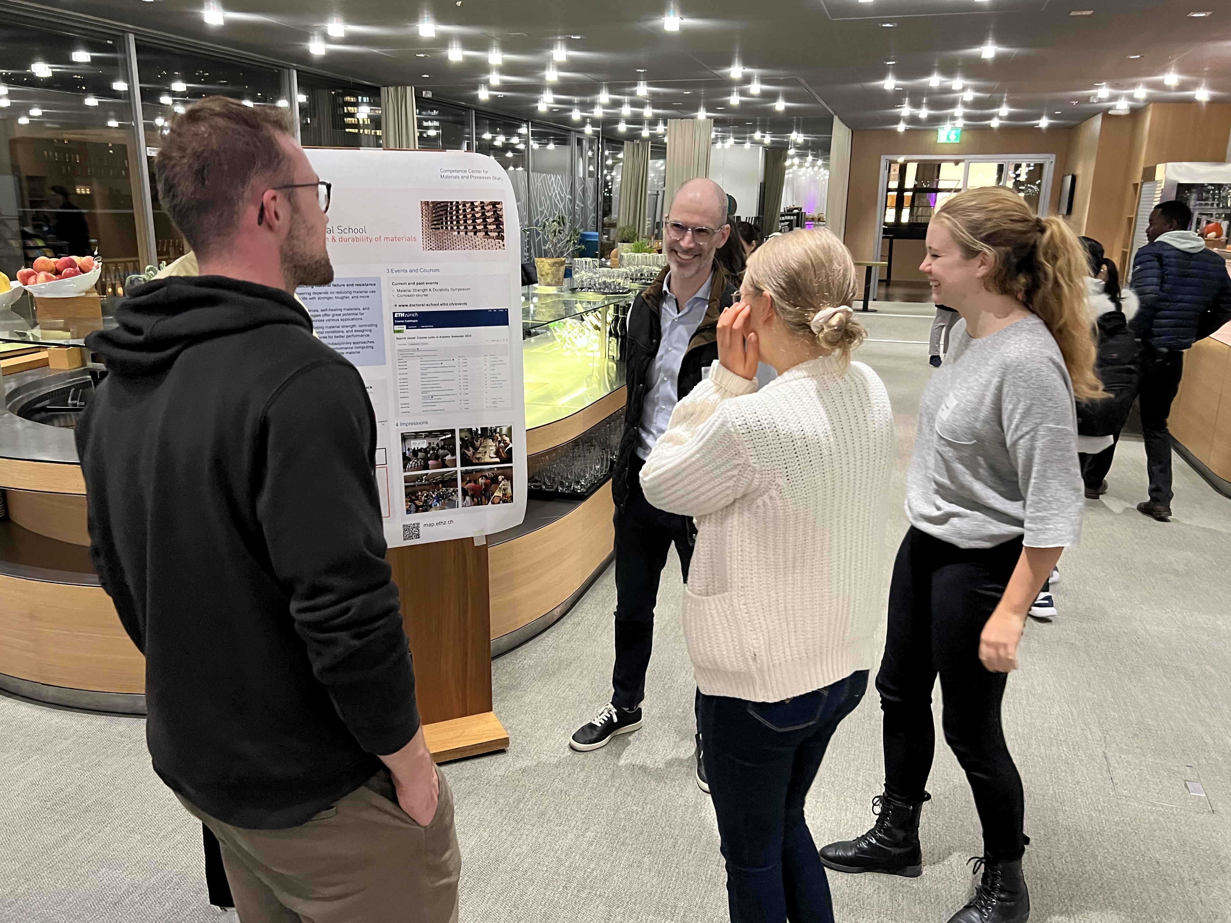 Prof. David Kammer and a group of 3 students discussing in front of one of the posters.