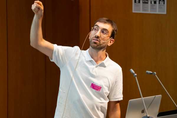 another presenter (a man in a white t-shirt) from chest up, pointing his finger up