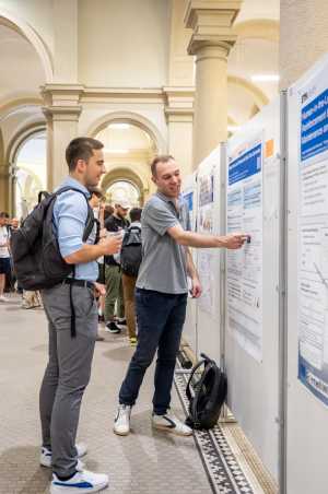 two guys in front of a poster, one pointing at something on it