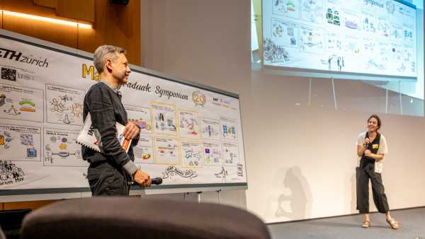 illustrator in front of his illustration, talking to the moderator (inside Audi Max)