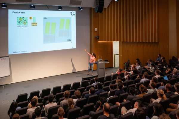 Lecture hall scene, presenter pointing to the screen