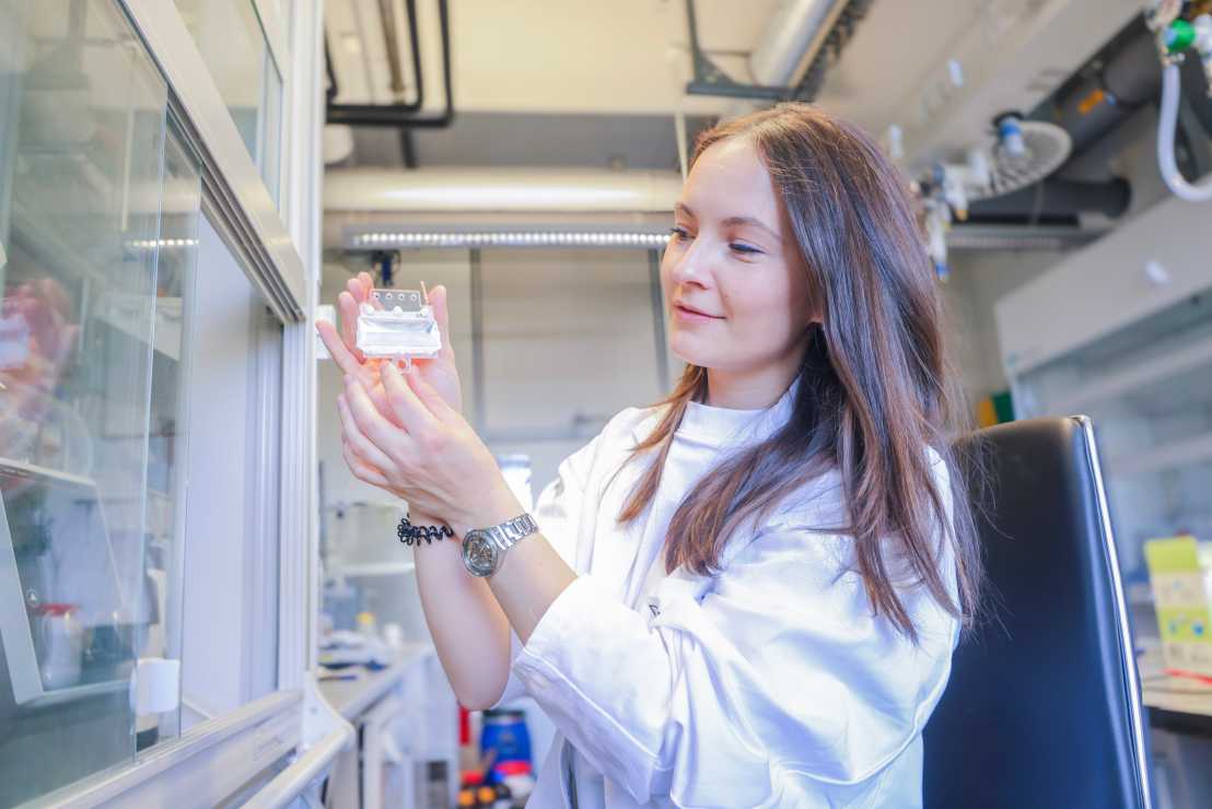 Daniela in a white lab coat in a lab setting, holding up