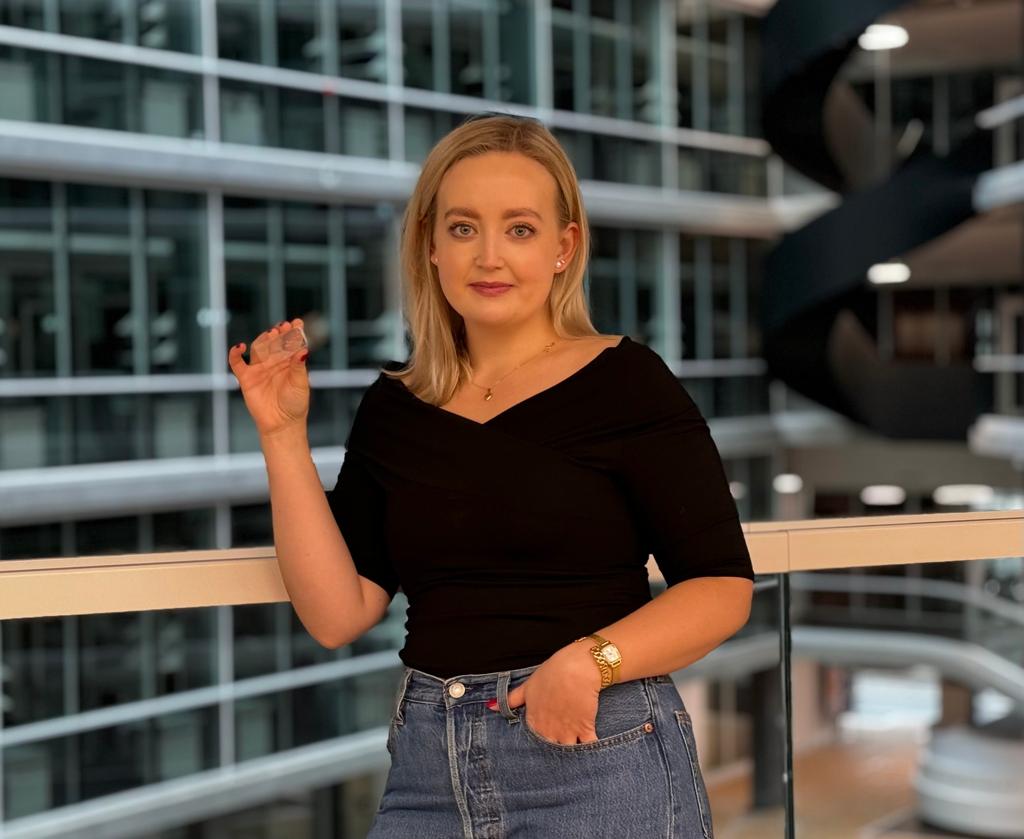 Portrait of a young woman standing in front of the banister inside the new D-BSSE building in Basel. She is holding up a small model.